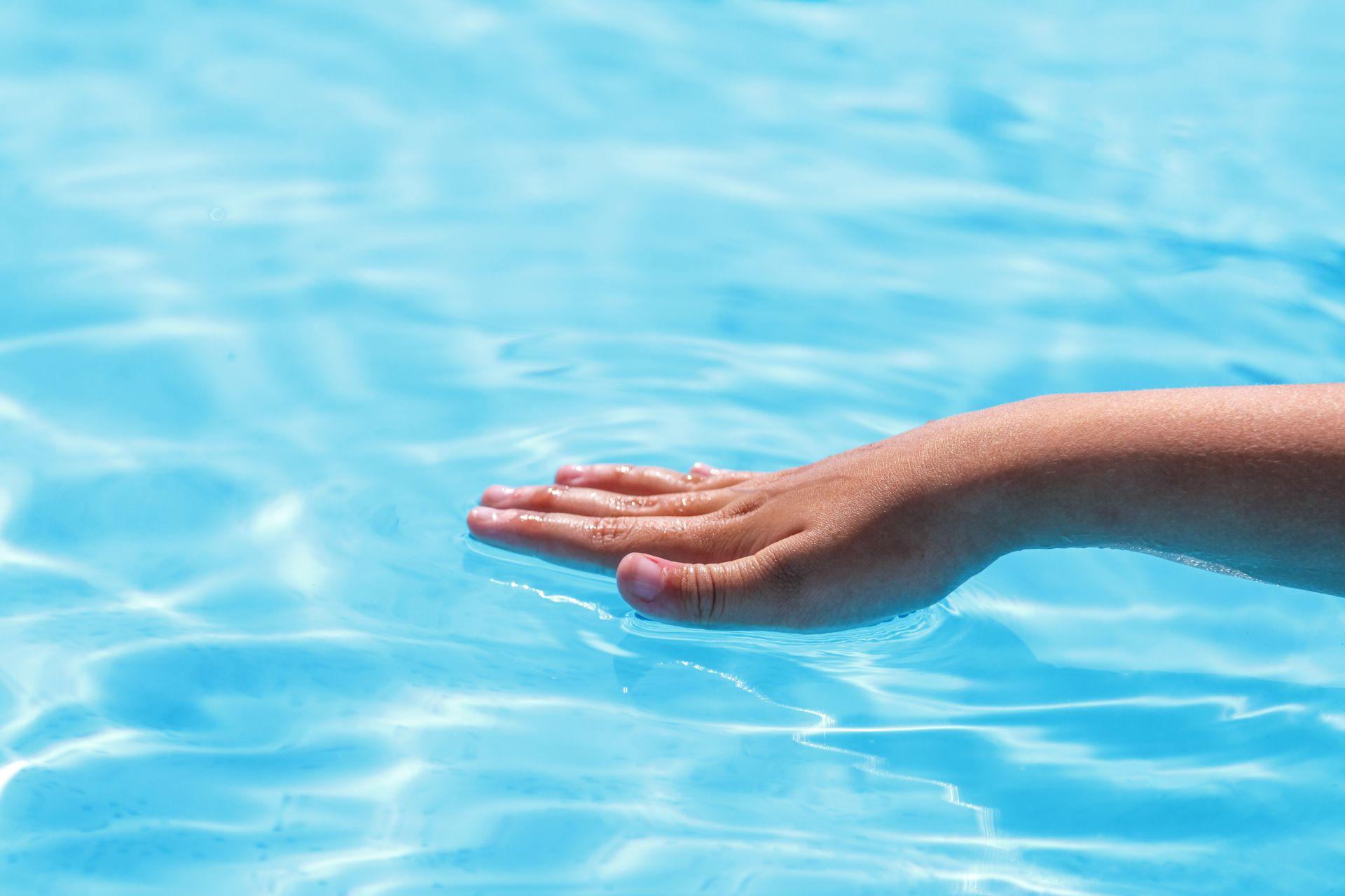 Kinderhand auf glatter Wasseroberflaeche – Symbolbild fuer hygienisch reines Poolwasser nach automatischer Reinigung